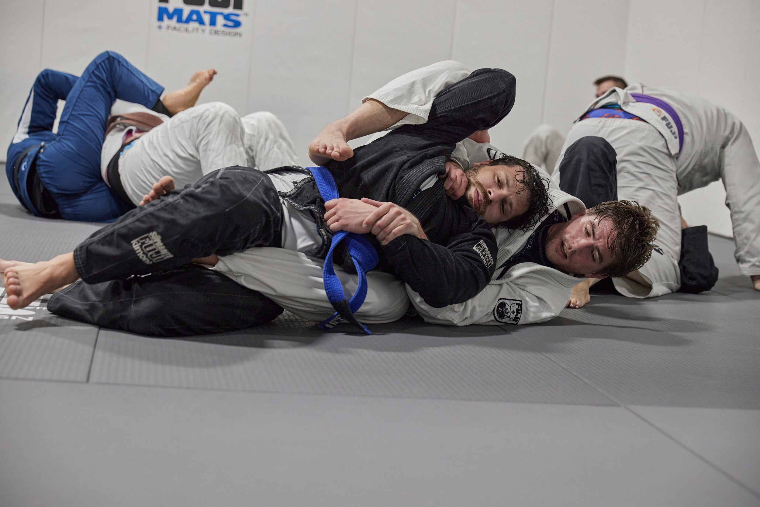 Two individuals practicing Jiu-Jitsu on a mat with 'MATS' branding in the background.
